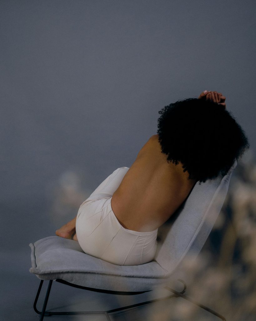 Artistic photograph of a woman posing shirtless on a chair with an elegant and moody background, depicting hurt as an invisible child (invisible child syndrome). Anonymous confession.