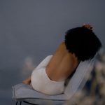 Artistic photograph of a woman posing shirtless on a chair with an elegant and moody background.